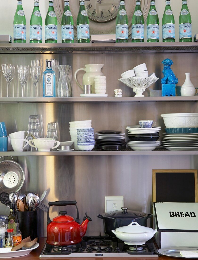 Crockery, glasses, ornaments and water bottles on wall-mounted shelving above hob
