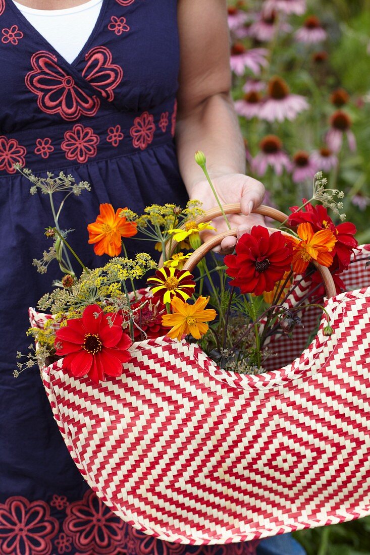 Frau sammelt Sommerblumen in einer Tasche