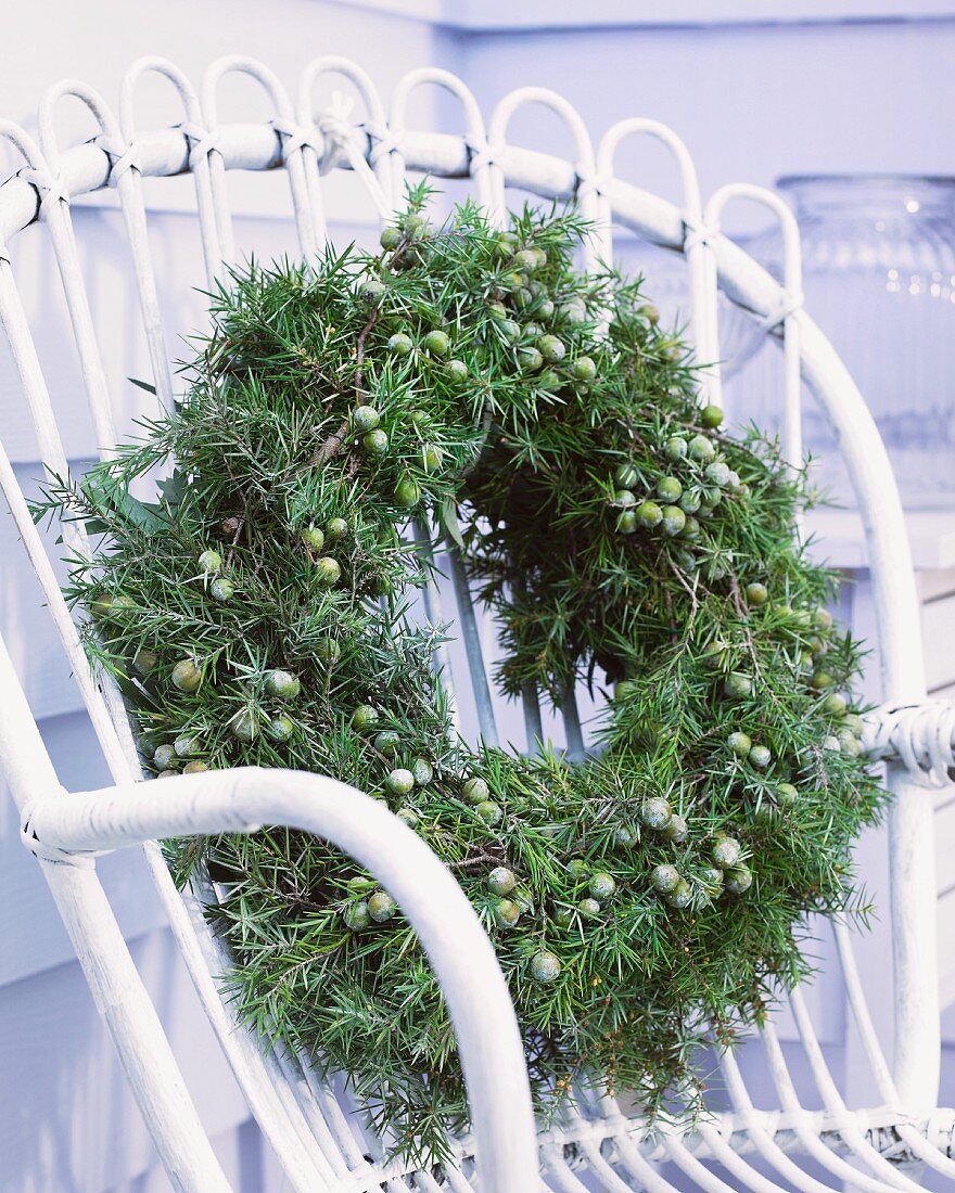 Winter wreath of juniper on white wicker chair on terrace