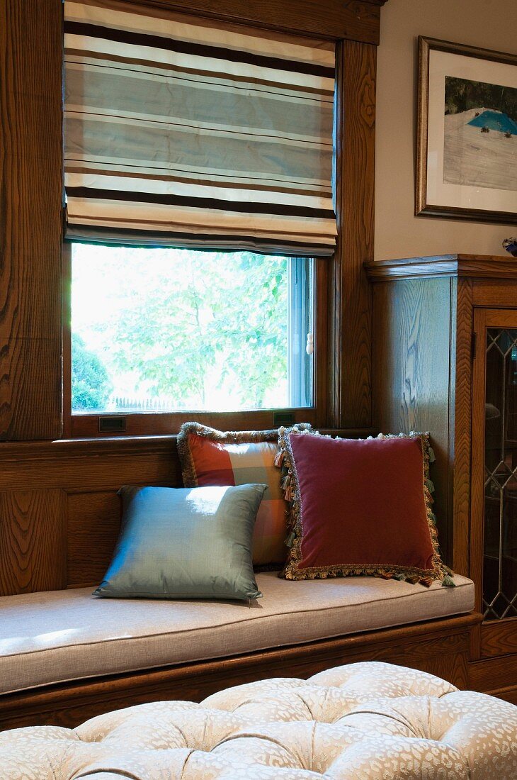 Cushions on built-in window seat at window with half-open blind