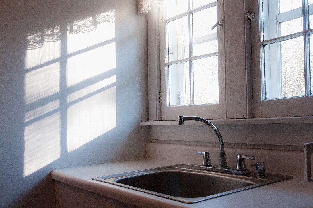 Old sink below window next to pattern of light and shadow on wall
