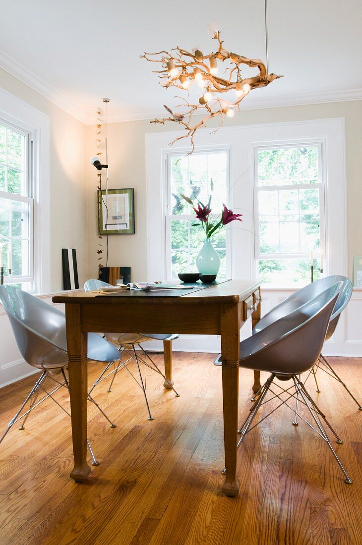 Rustic wooden dining table and pale grey plastic shell chairs below pendant lamp crafted from roots