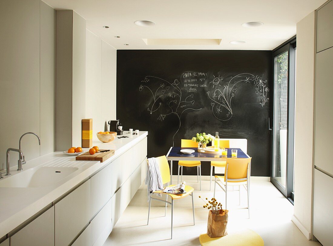 Restrained, modern kitchen counter with Corian counter top and colorful dining area in front of a chalkboard wall