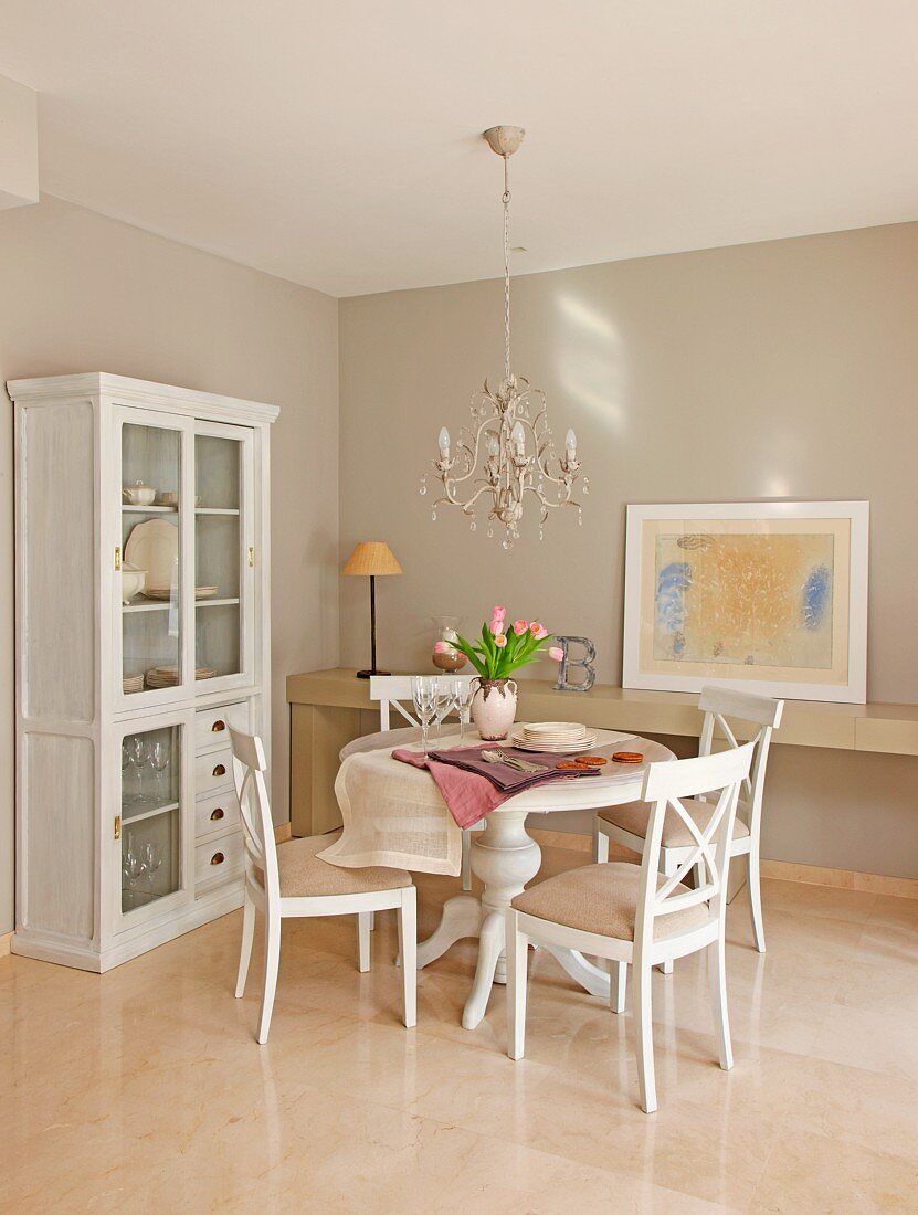 Dining area with chandelier and white, glass-fronted, country-house-style cabinet
