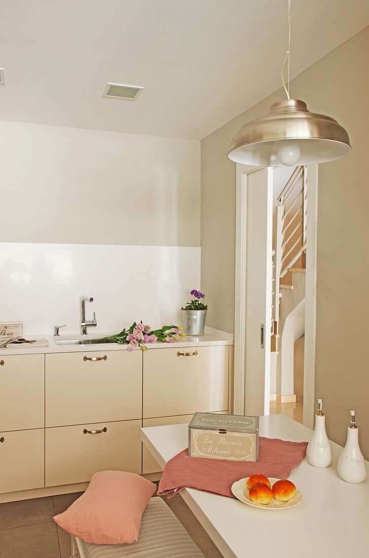 Breakfast area with dusky pink accessories and industrial-style retro lamp; fitted kitchen with pale beige fronts in background