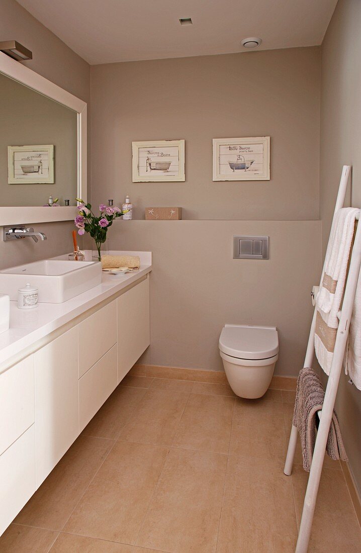 Schmales Bad mit langgestrecktem Waschtischschrank und Handtuchleiter vor warmgrau getönten Wänden
