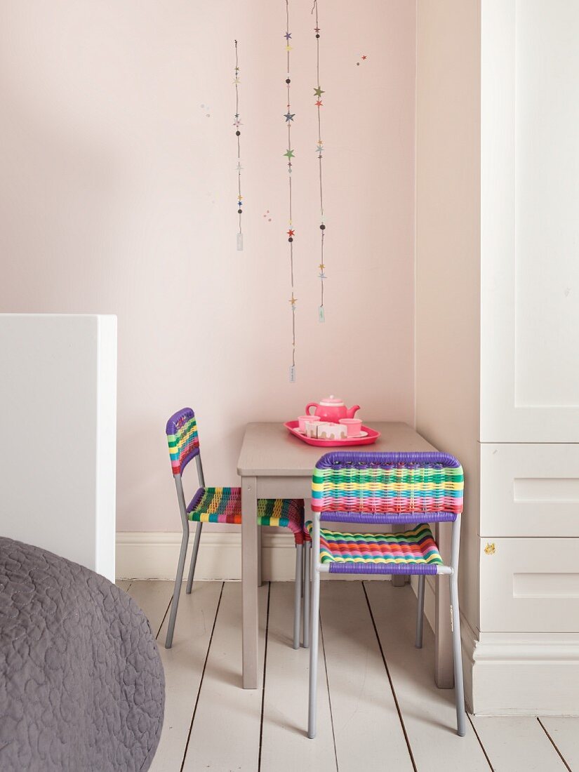 Sitzplatz mit bunten Flechtstühlen und rosa Kaffeegeschirr im Kinderzimmer