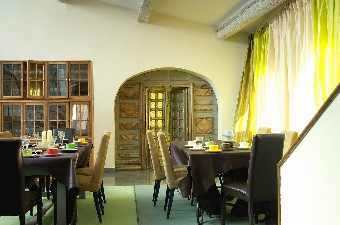 Frühstückszimmer mit Gedecken auf Tischen und Blick durch Rundbogen auf Verzierung um Tür mit Glasfüllung
