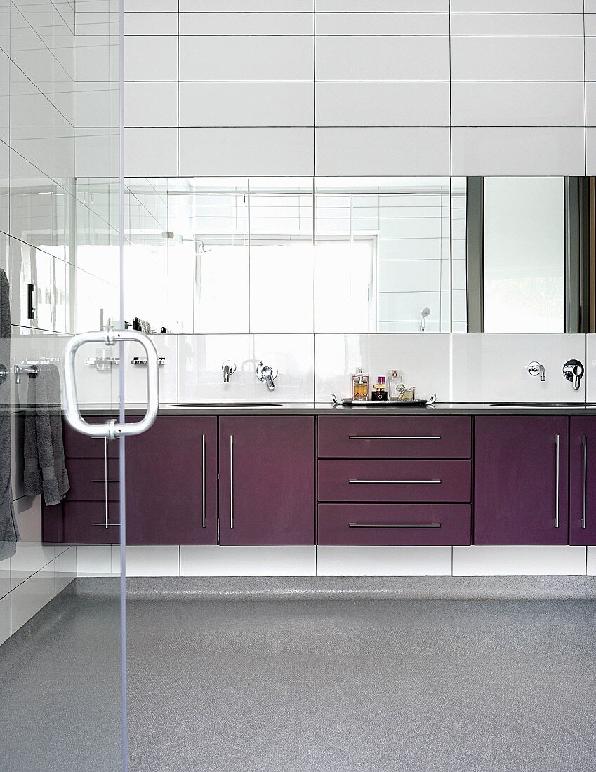 Waschtischzeile mit violetten Schrankfronten und Spiegelband auf weissen Wandfliesen