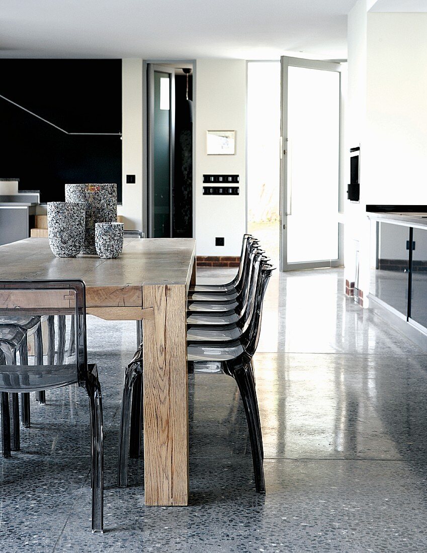 Massiver Holztisch mit Plexistühlen als Essplatz gegenüber einer Küchenzeile
