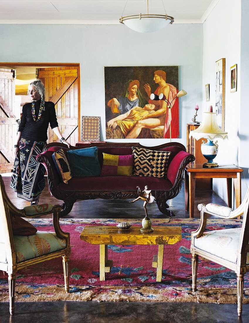 Interior in eclectic mixture of styles with antique seating and collection of unusual objet; woman leaning on sofa