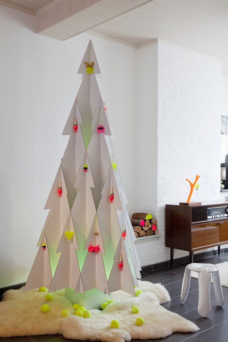 Stylised Christmas tree made from white cardboard with decorations in neon yellow and pink on white fur rug