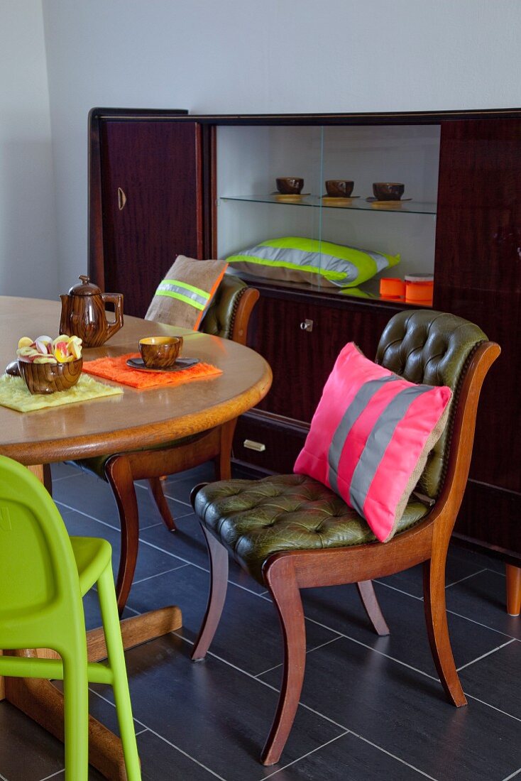 Tasteful dining area with neon striped cushions, retro glass-fronted cabinet and green high chair in foreground