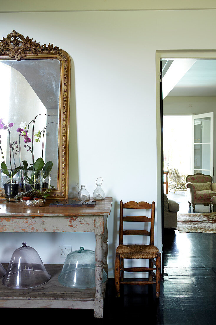 Orchideen und goldgerahmter Spiegel auf altem Holztisch, daneben Blick ins Wohnzimmer mit traditionellen Polstersesseln