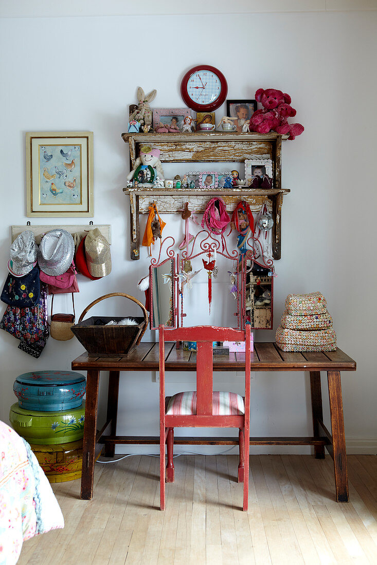 Girlish collection of soft toys, hats and bags on rustic wooden table with pink-painted wooden chair