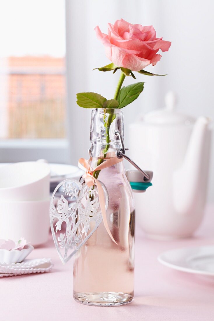Rose in bottle used as vase with heart-shaped pendant