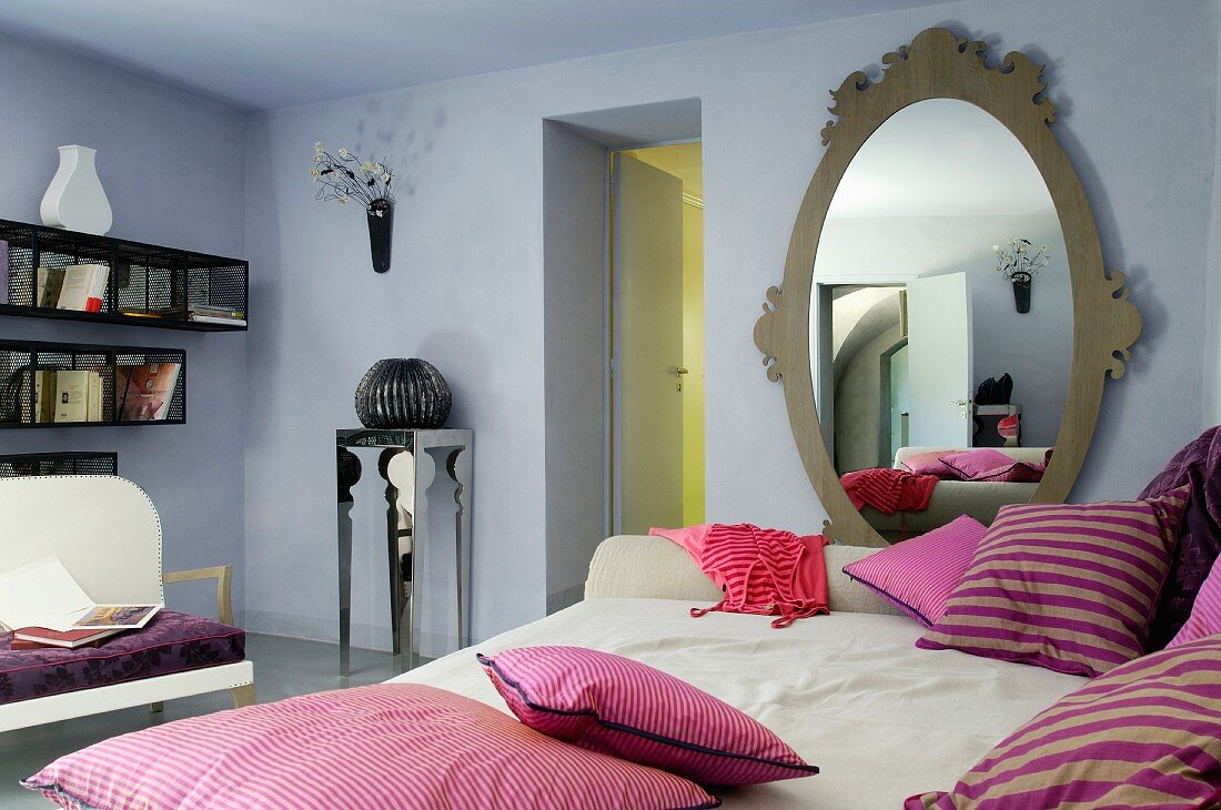 Liege mit violett gestreiften Kissen, Ovalspiegel in hellblau getöntem Wohnraum
