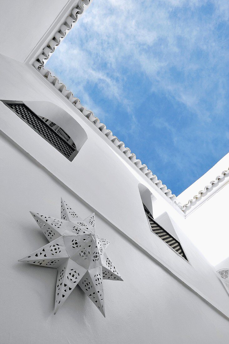 Upwards view of blue and white sky from Moroccan courtyard; star-shaped console lamp made from pierced metal