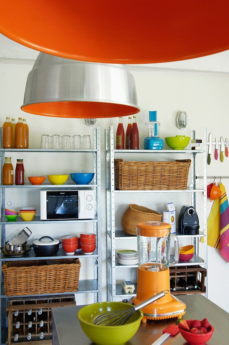 Orangefarbene Industrieleuchten und Metallregale in einfacher Küche mit bunten Küchenutensilien