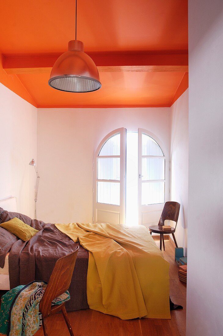 Schlichte Industrieleuchte in schmalem Schlafraum mit knallig orangefarben gestrichener Decke