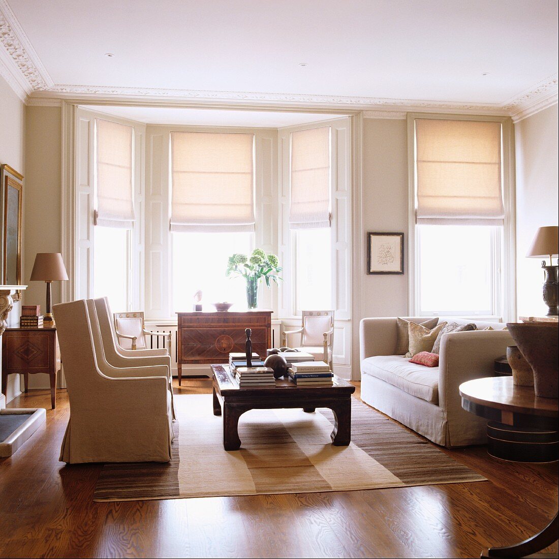 Living room: elegant, light colored furniture with a bay window and half-closed Roman blinds at the windows