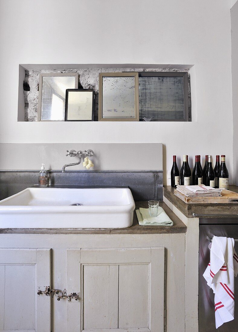Collection of mirrors in niche above vintage sink on grey base unit in simple interior