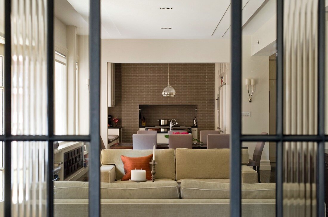 View though half-open, glass sliding doors into lounge area with pale sofa set and dining area against brick wall
