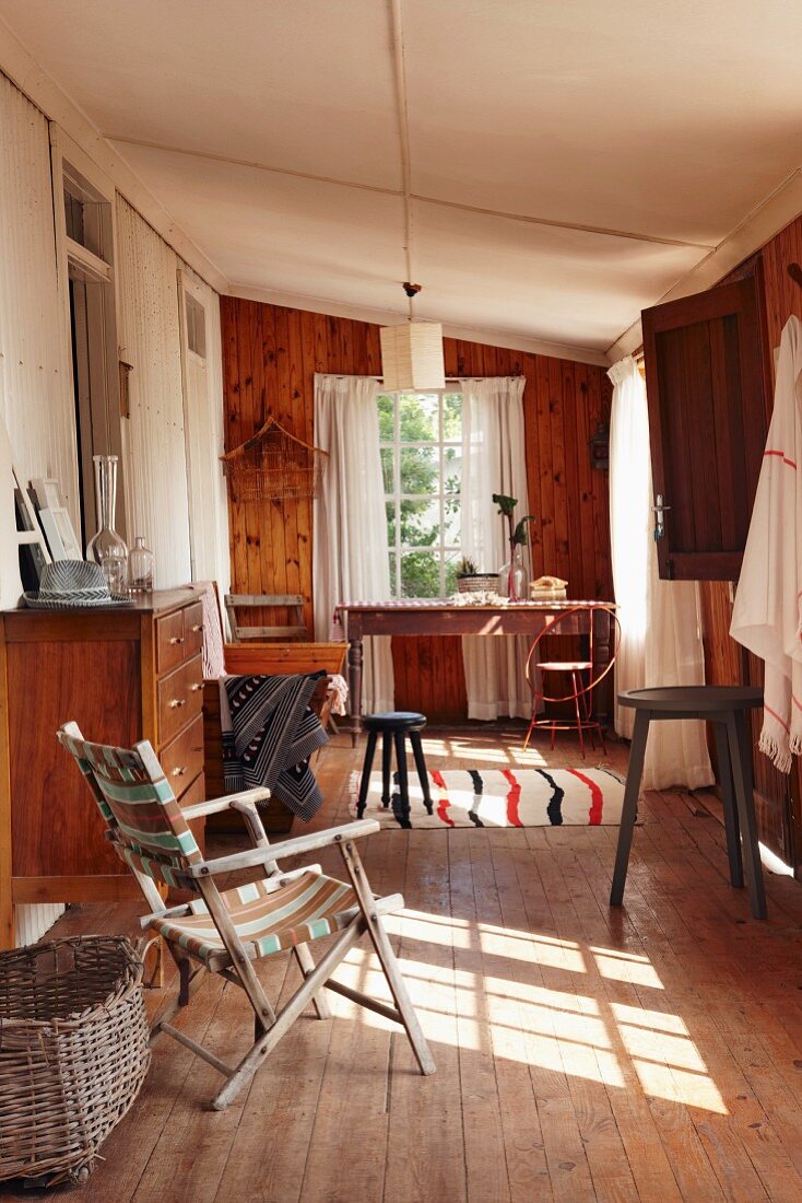 Verschiedene Vintage Möbel in schmalem Raum mit Holzvertäfelung, weissen Metallprofilen und Dielenboden