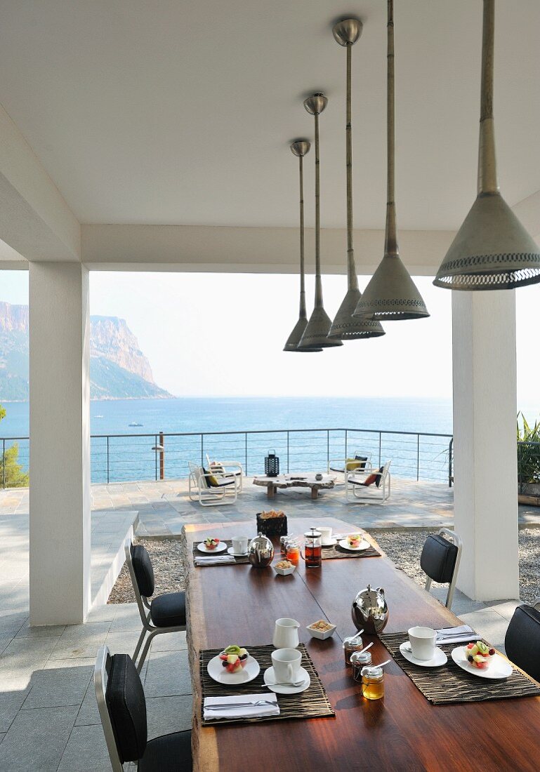 Stylish place settings on table on roofed terrace with sea view