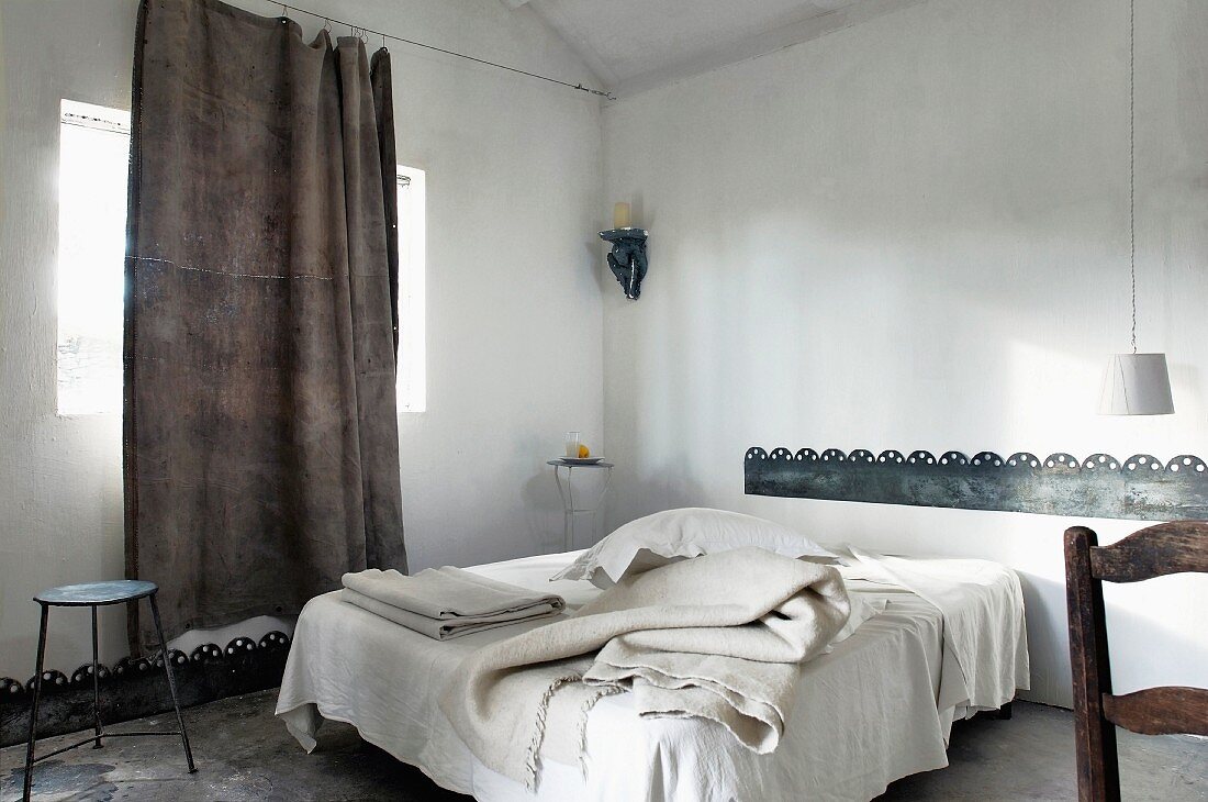 Verschiedene Bettdecken auf französischem Bett, lässiger Leinenvorhang an gespanntem Drahtseil und Blechstreifen als Wandbordüre