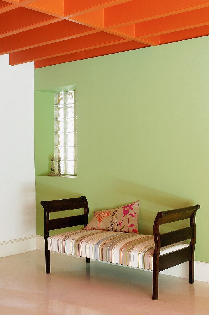 Orangerot gestrichene Deckenbalken über einer Recamiere vor grüner Wand