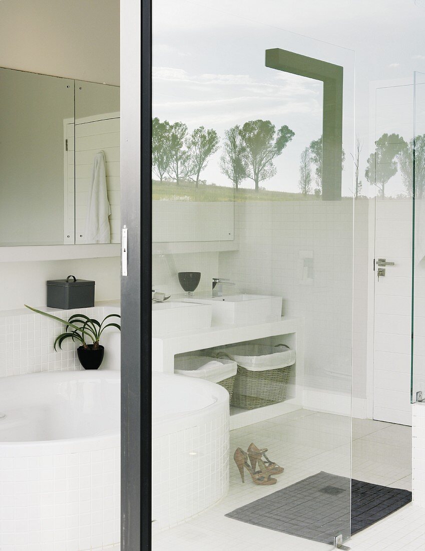 Blick durch Glaswände in weisses Bad mit runder Wanne; Spiegelung der umgebenden Natur auf Glaselement