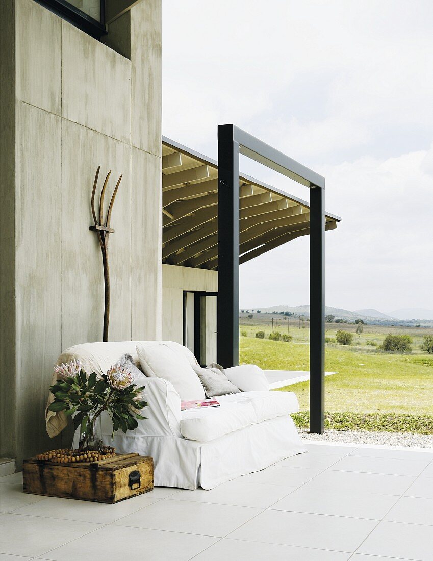 Terrace of a home located in an open landscape with an inviting sofa and crate table in front of an exposed concrete wall