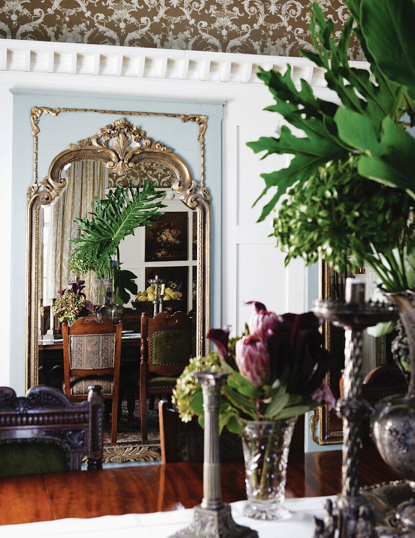 Blumen in Vase auf Tisch gegenüber verziertem Wandspiegel mit Reflexionen