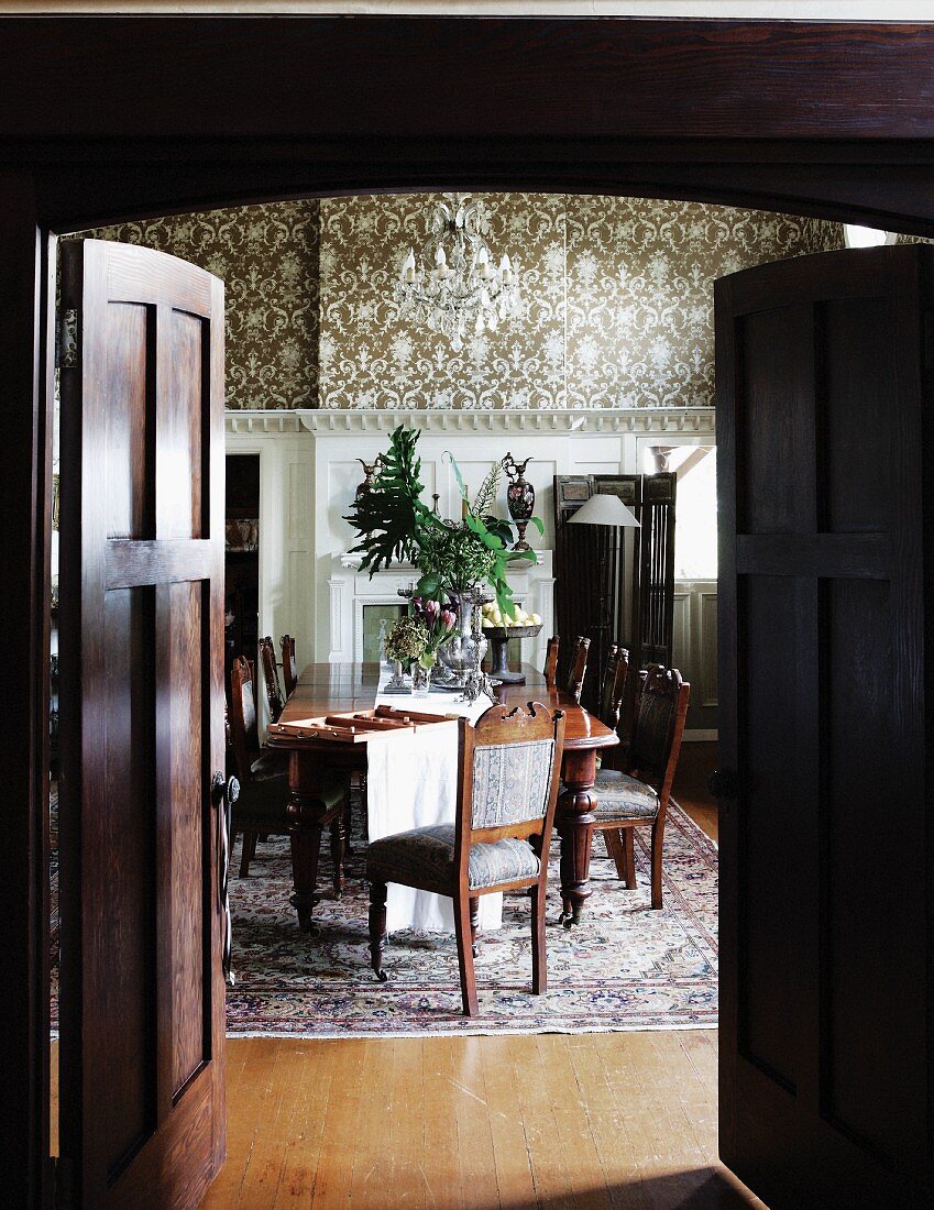 Blick durch offene Flügeltür aus dunklem Holz in traditionelles Esszimmer mit langer Esstafel und antiken Stühlen im Kolonialstil