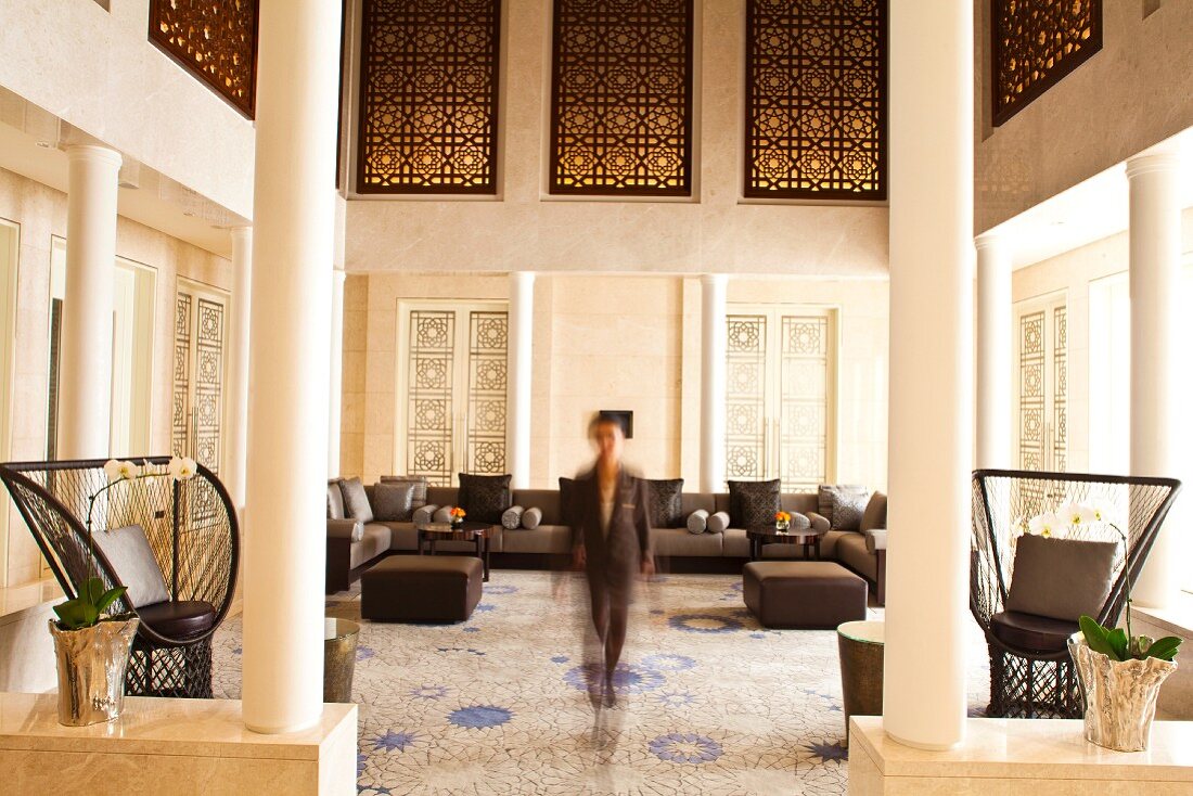 Blick durch Säulen-Entree auf Frau in elegantem Foyer mit Loungebereich