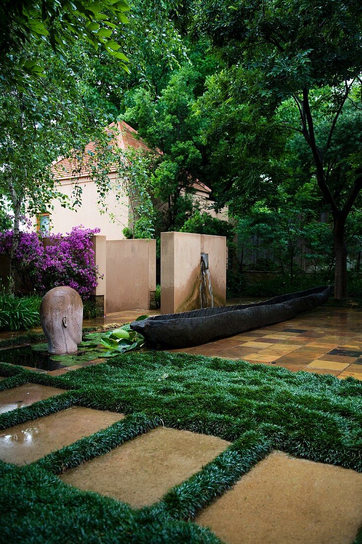 Künstlerisch angelegter Garten mit Objekten und Grasflächen neben gefliesten Flächen