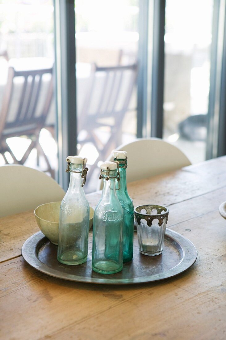 Vintage swing-top bottles on tray and rustic wooden table in front of terrace window
