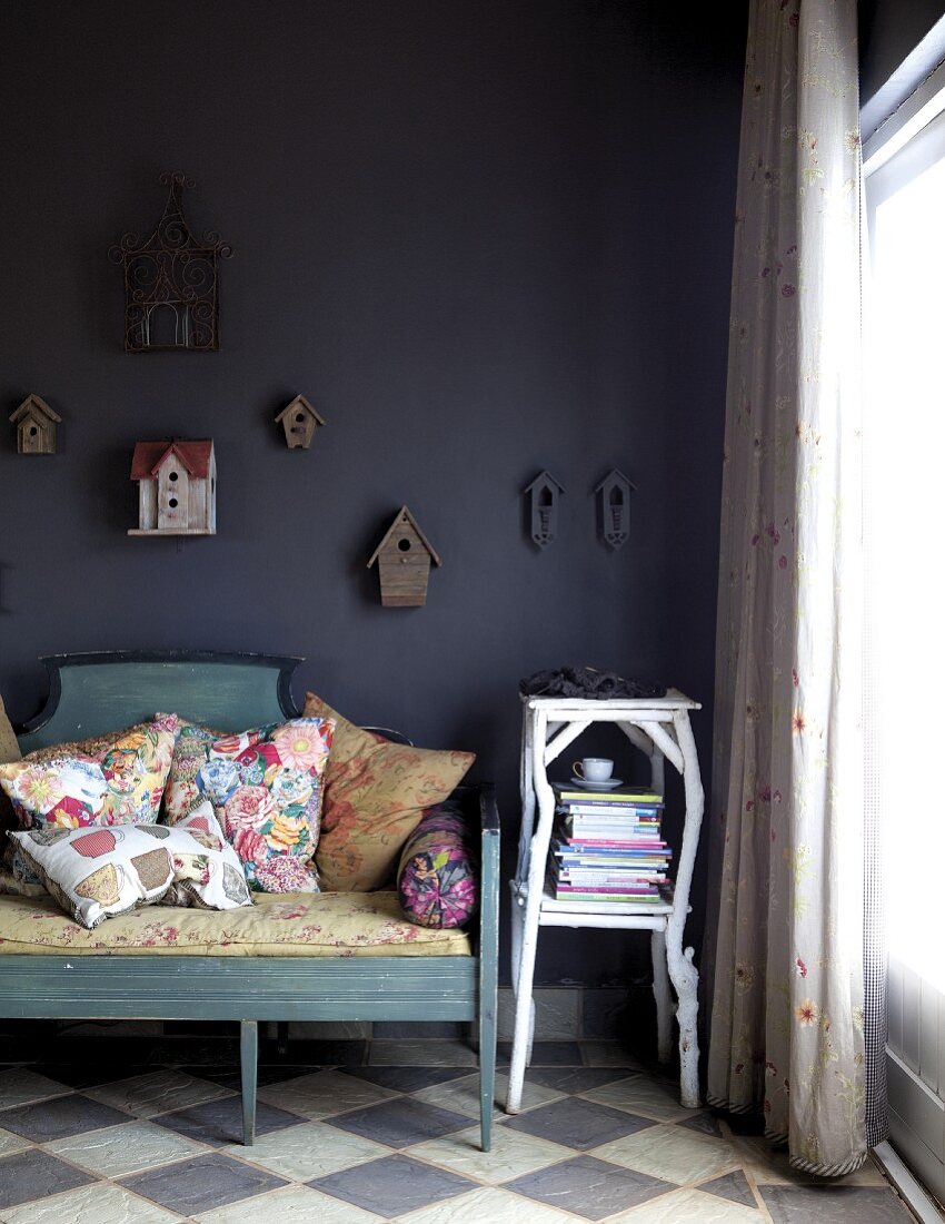 Vintage Sitzbank mit bunten Kissen neben Beistelltisch aus Ästen vor dunkler Wand