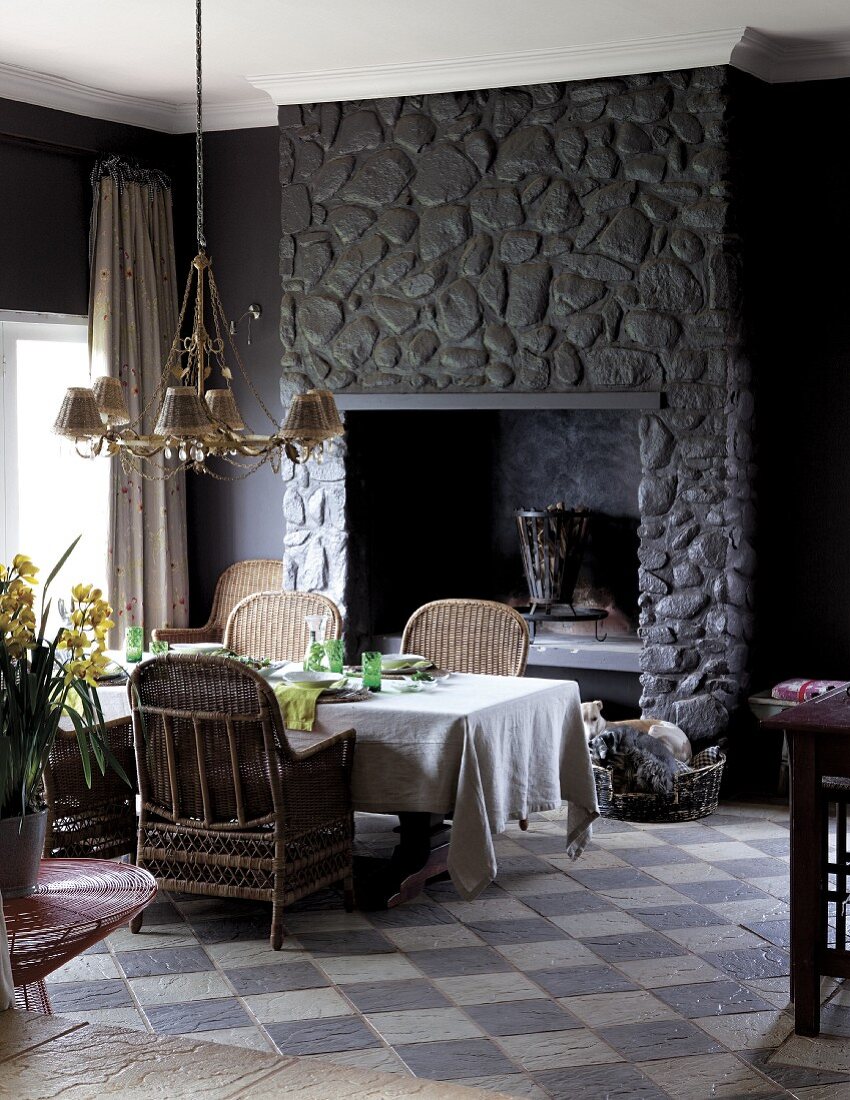 Esstisch vor Kamin in dunkler Natursteinwand und Schachbrettmusterboden im Vintagestil