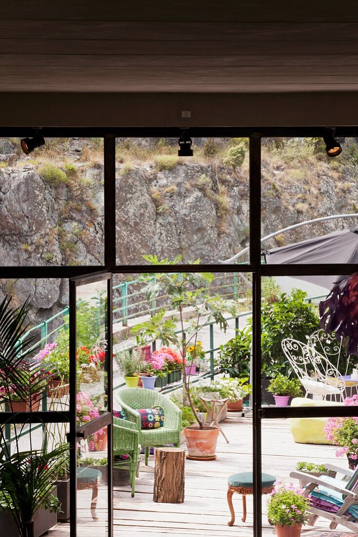 Blick durch offene Tür in raumhoher Industrieverglasung auf rampenartige Terrasse mit Sitzmöbeln und Topfpflanzen
