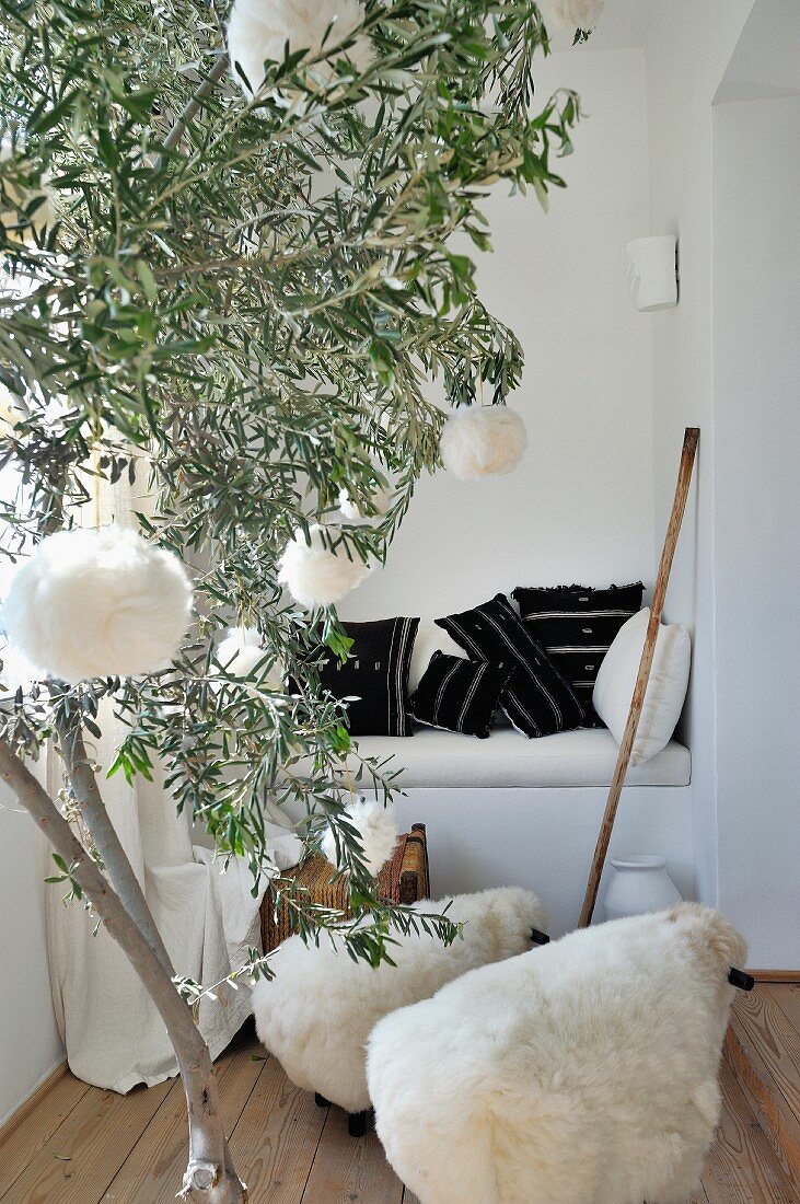 Olivenbaumstamm mit Wollkugeln und Schäfchenhocker vor gemauerter Sitznische mit schwarzweiss gewebten Kelimkissen
