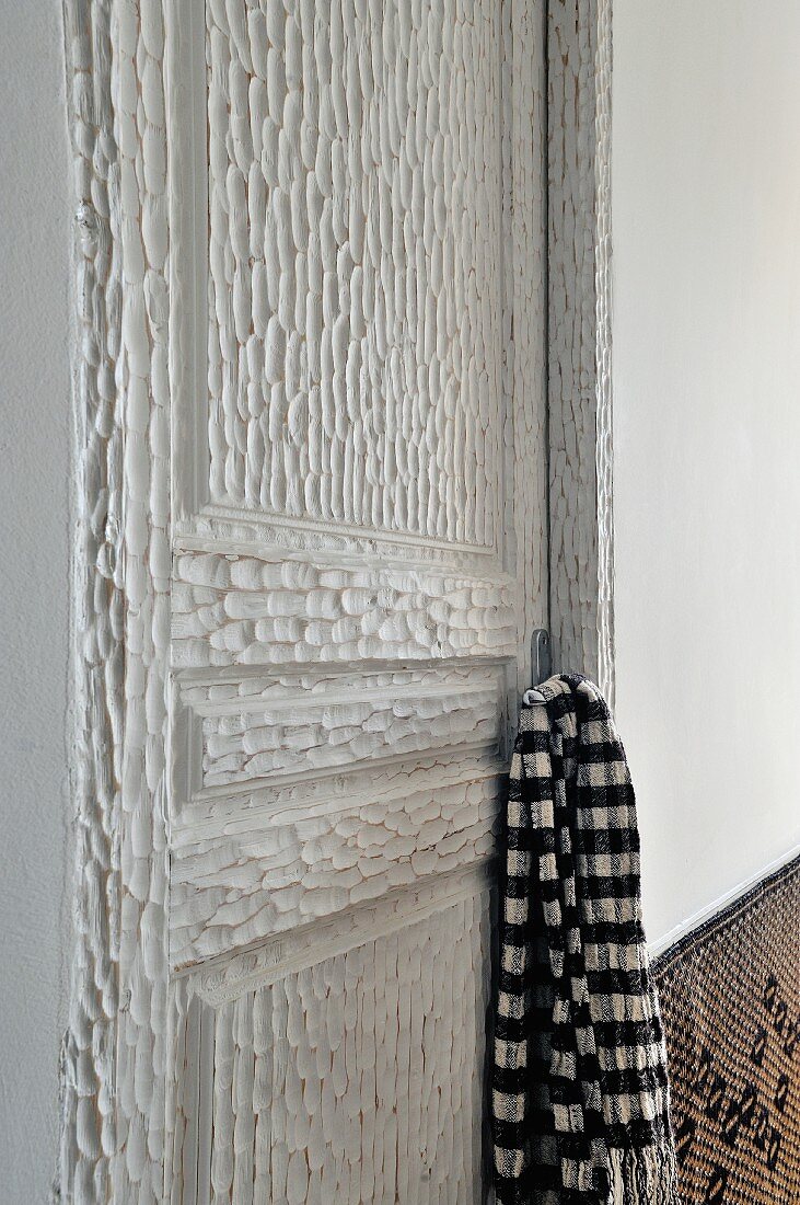 Schwarzweisses Schaltuch am Griff einer kunsthandwerklich bearbeiteten, weiss lackierten Holztür