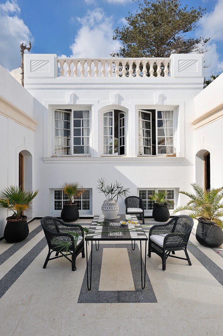 Schwarzweiss gestalteter Innenhof im nordafrikanischen Stil mit Korbstühlen an Mosaiktisch und Palmentöpfen