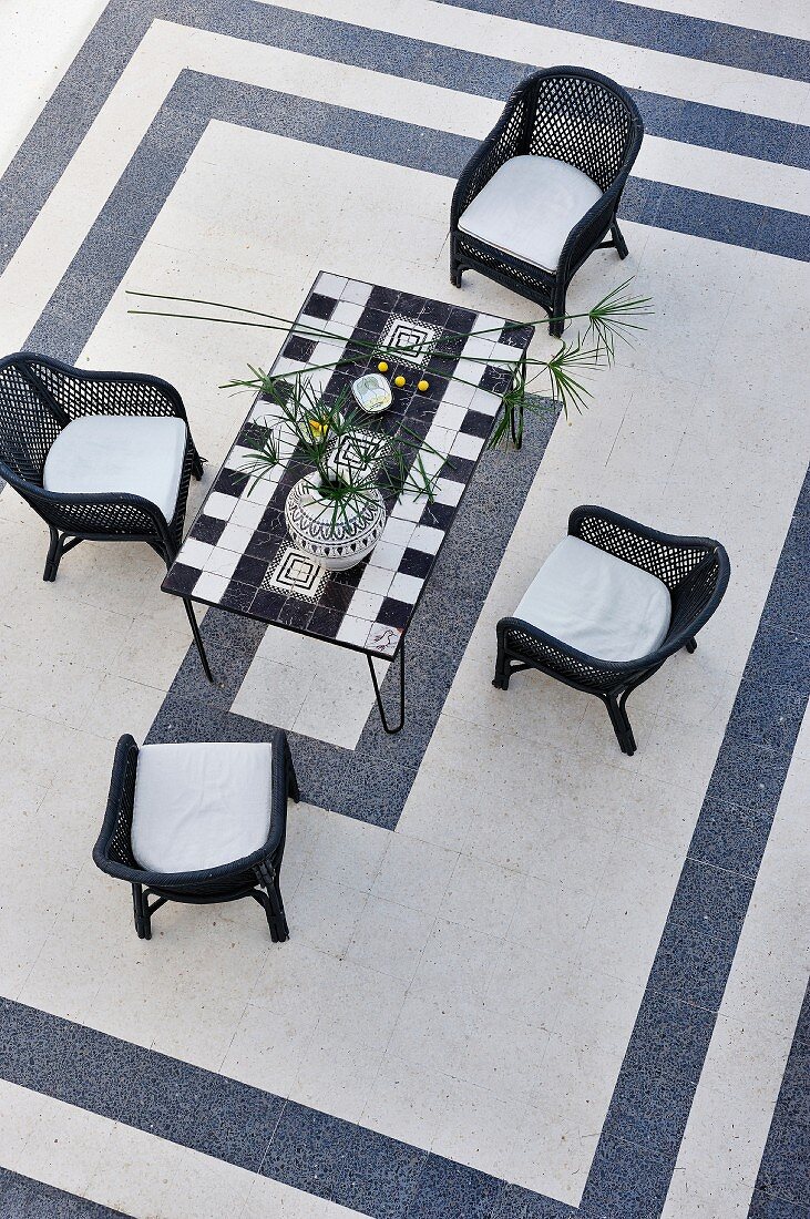 Wicker chairs around a mosaic table and black and white tile patterns (top view)