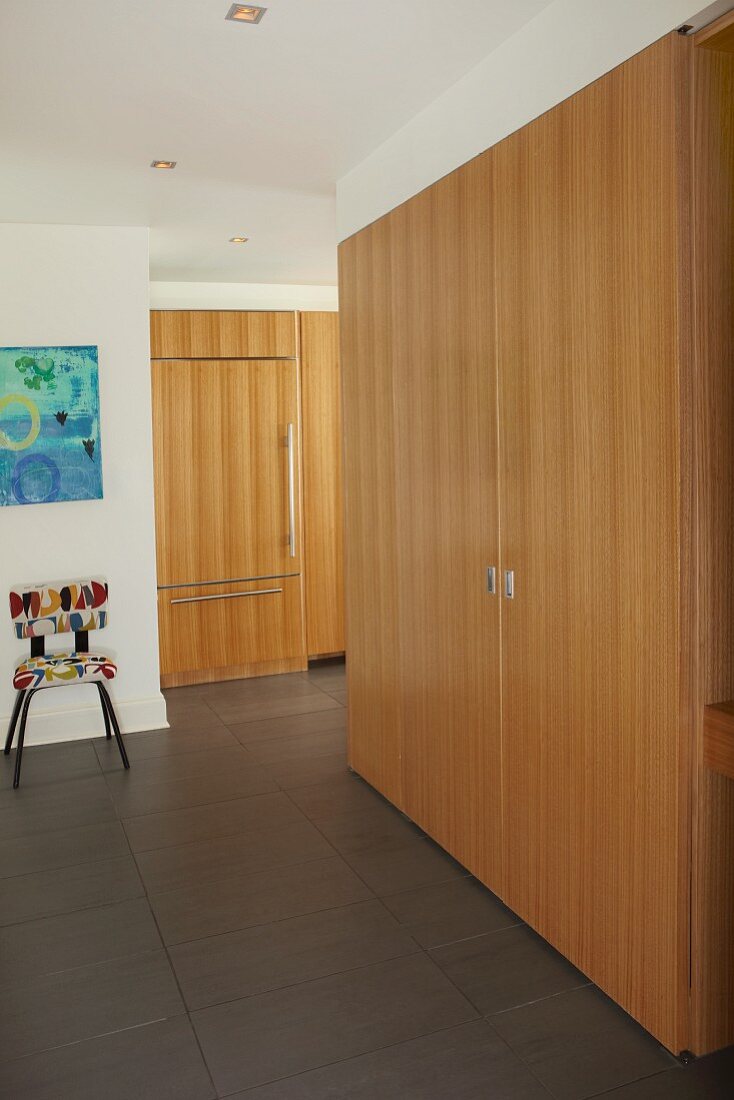 Einbauschrank aus Holz in modernem Flur und Blick in offene Küche mit gleicher Holzfront