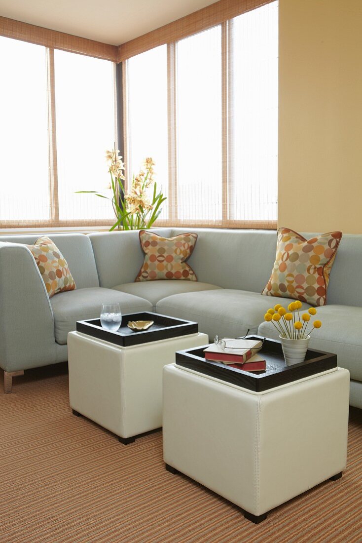 Comfortable seating corner with pale grey upholstery and cubic side tables with white leather covers below window