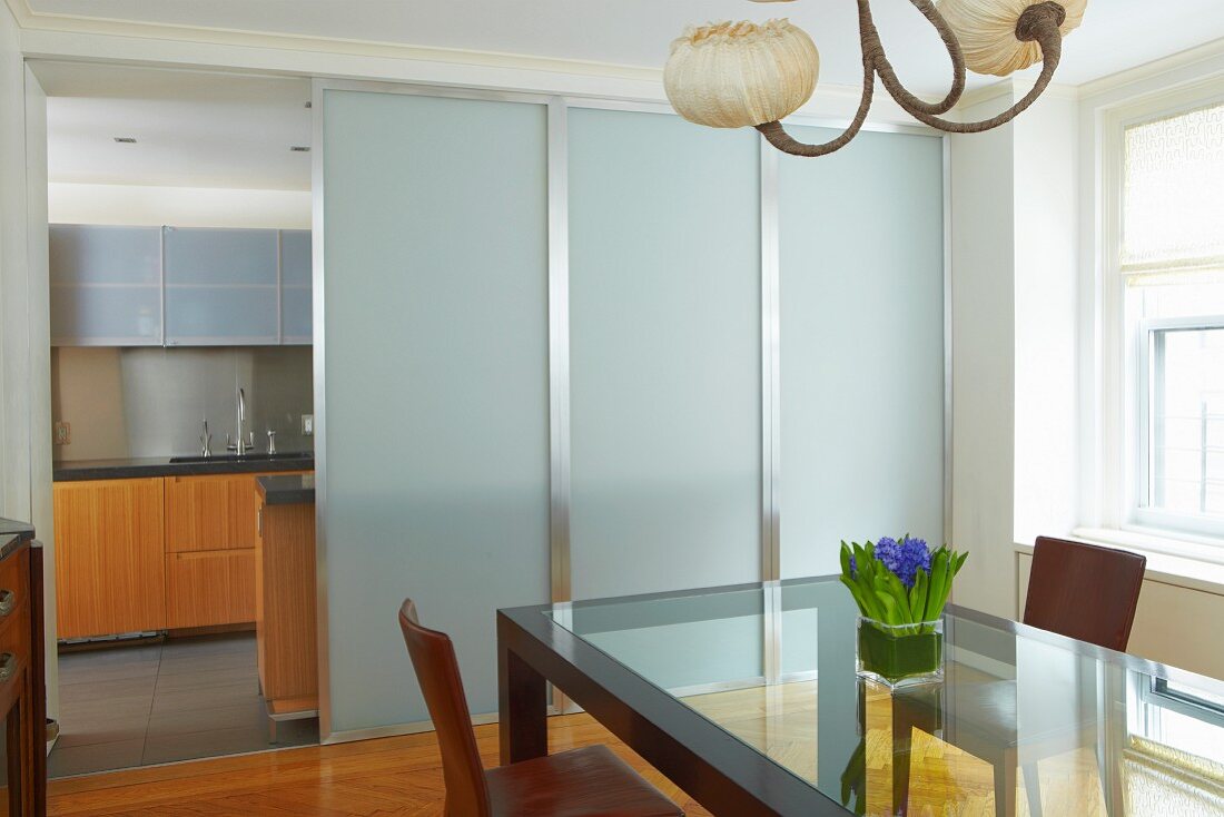Essplatz vor modernen Schiebeelementen aus Glas und Stahl und Blick durch Öffnung in die Küche