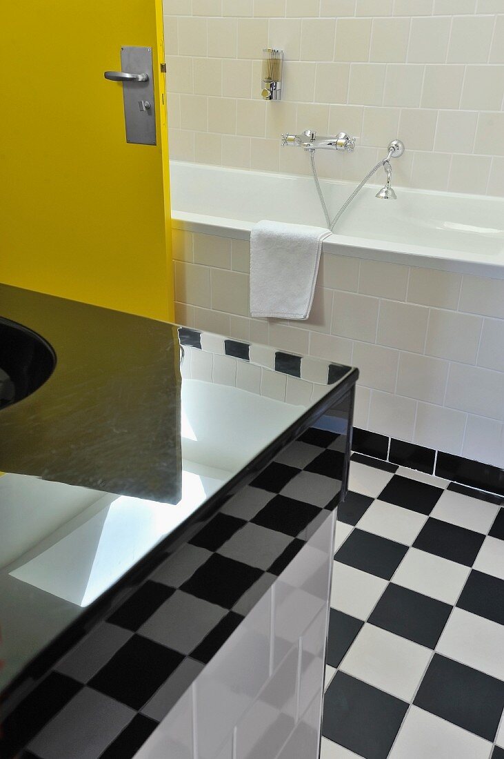 Modernes Bad mit Retro-Touch, teilweise sichtbarer Waschtisch mit hochglänzender Oberfläche und gelbe Tür im Bad mit schwarz-weißem Schachbrettboden