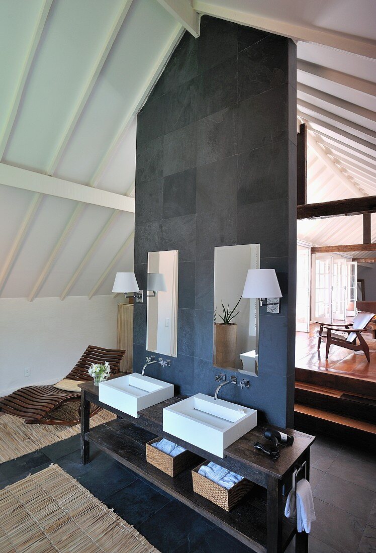 Open bathroom vanity area in a renovated attic - vanity on the room divider with gray slate counter top in front of wooden stairs leading to another level